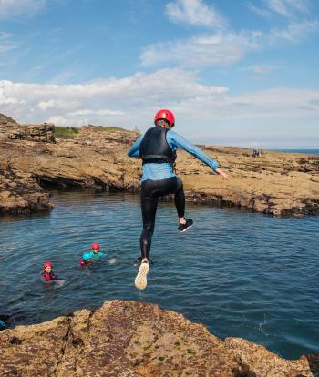 Group of people jumping into sea on coasteering trip in Devon