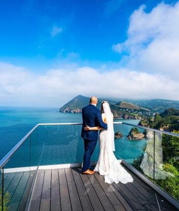 A bride and groom standing on the platform at The Venue, Sandy Cove, looking at the view of the bay