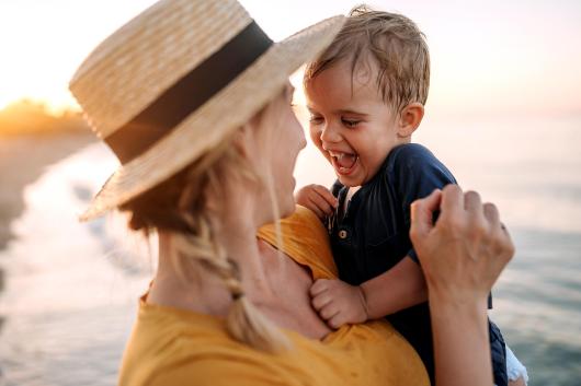 A mum holding her smiling toddler son after a swim in the sea