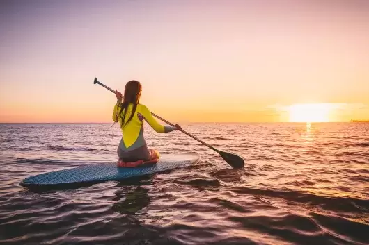 A paddleboarder kneeling on her board on calm seas at sunset