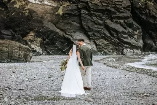 A groom whispering to his new wife as they walk along the beach near Sandy Cove Hotel after their wedding