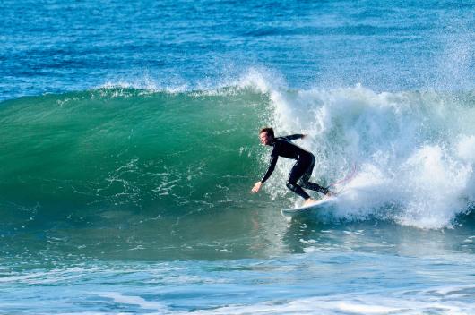 Surfer leaning into a bottom turn on a sunlit wave in North Devon